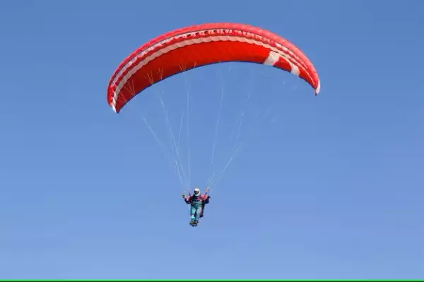 Человек летит под красным парапланом на фоне голубого неба